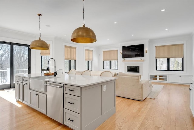 kitchen featuring decorative light fixtures, light wood-style flooring, stainless steel dishwasher, a glass covered fireplace, and a sink