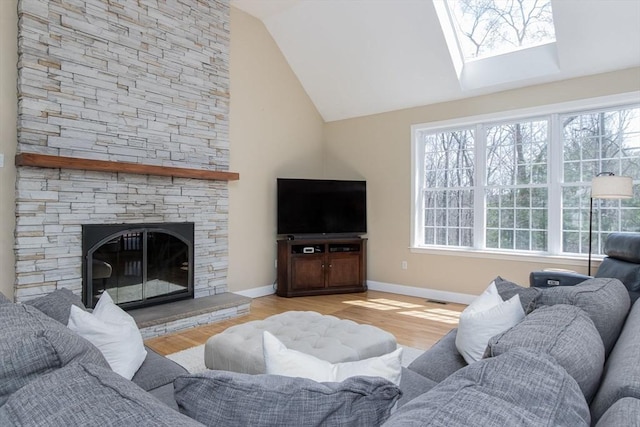 living room with vaulted ceiling with skylight, baseboards, a stone fireplace, and wood finished floors