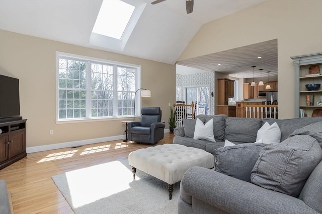 living area featuring vaulted ceiling with skylight, baseboards, ceiling fan, and light wood-type flooring