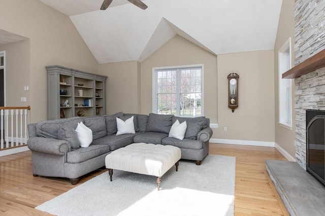 living room featuring lofted ceiling, a stone fireplace, baseboards, ceiling fan, and light wood-style flooring