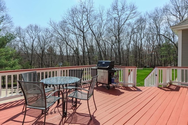 deck featuring a view of trees, outdoor dining space, and a grill