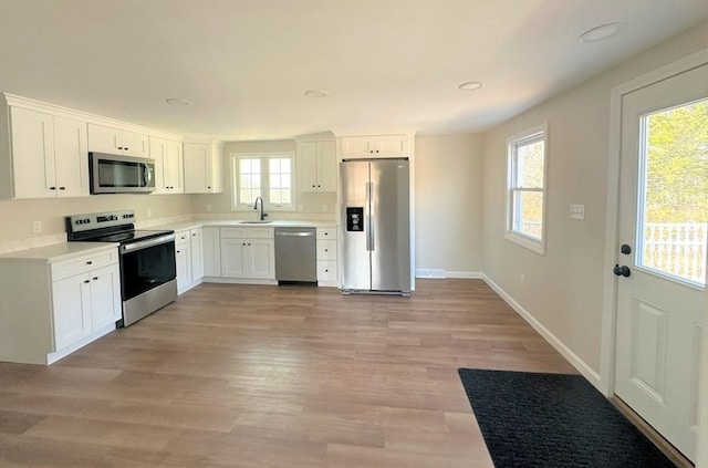 kitchen with a sink, stainless steel appliances, baseboards, and white cabinets