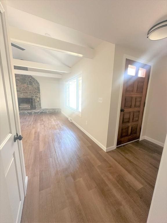 entryway featuring lofted ceiling with beams, baseboards, a stone fireplace, and wood finished floors