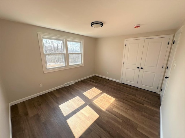 unfurnished bedroom with a closet, visible vents, dark wood-type flooring, and baseboards