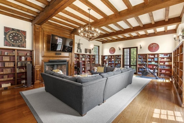 living area with a large fireplace, wood-type flooring, beamed ceiling, and a chandelier
