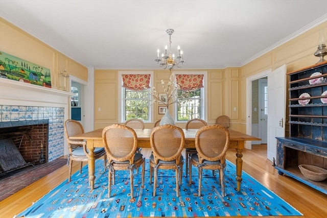 dining room with an inviting chandelier, wood finished floors, a tiled fireplace, a decorative wall, and ornamental molding