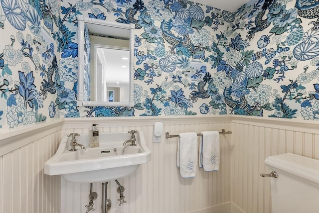 bathroom featuring toilet, wainscoting, and wallpapered walls