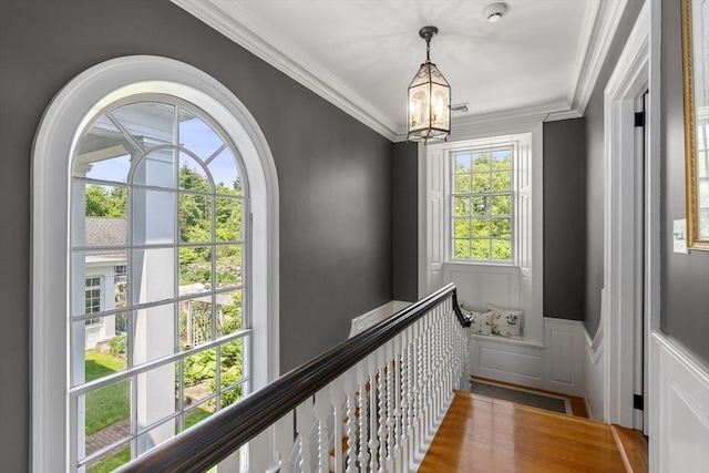 hallway with a wainscoted wall, a notable chandelier, visible vents, a decorative wall, and ornamental molding