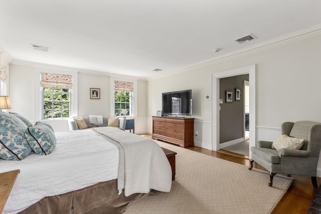 bedroom with baseboards, crown molding, visible vents, and wood finished floors