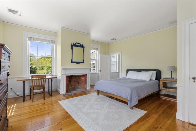 bedroom featuring multiple windows, light wood-style floors, visible vents, and a fireplace with flush hearth