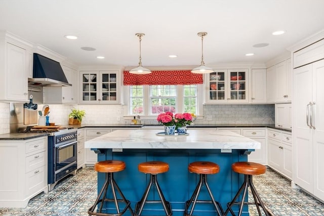 kitchen featuring high end stove, a breakfast bar, white cabinetry, wall chimney range hood, and tasteful backsplash