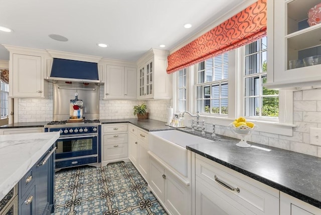 kitchen with white cabinetry, a sink, wall chimney exhaust hood, and tasteful backsplash