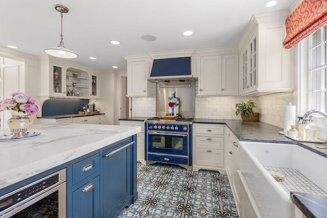 kitchen featuring a sink, range with two ovens, white cabinets, decorative backsplash, and custom exhaust hood