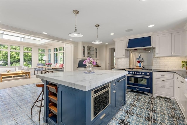 kitchen featuring double oven range, wall chimney exhaust hood, a kitchen island, blue cabinetry, and white cabinets