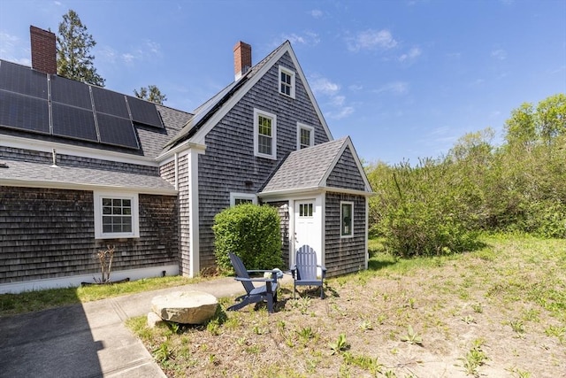 831 Main St, Dennis, MA 02638 - rear view of house with solar panels, a shingled roof, a chimney, and an outbuilding