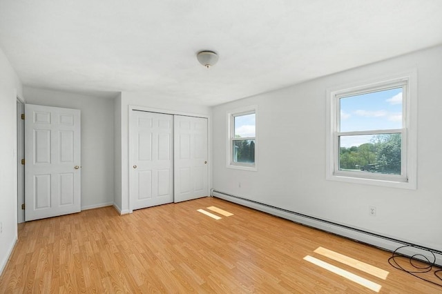 unfurnished bedroom featuring a baseboard heating unit, light wood finished floors, a closet, and baseboards
