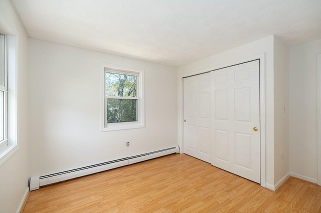 unfurnished bedroom featuring a baseboard heating unit, light wood finished floors, a closet, and baseboards