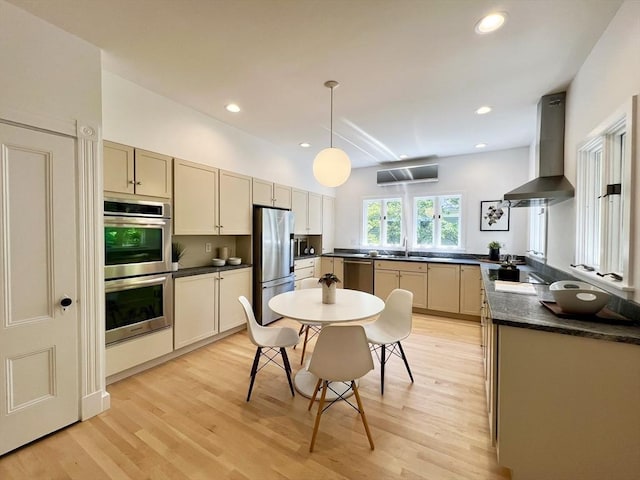 kitchen featuring stainless steel appliances, wall chimney exhaust hood, dark countertops, light wood-style flooring, and pendant lighting