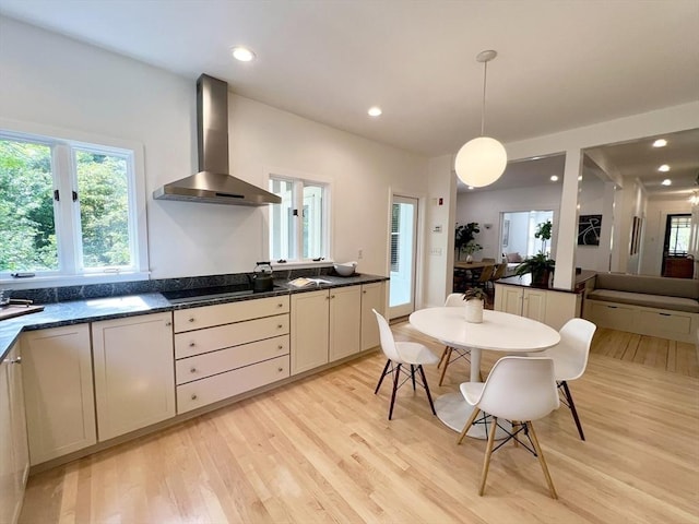 kitchen featuring wall chimney range hood, light wood-style flooring, dark countertops, black electric stovetop, and decorative light fixtures