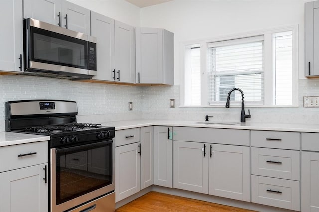 kitchen featuring light hardwood / wood-style flooring, sink, gray cabinets, tasteful backsplash, and appliances with stainless steel finishes