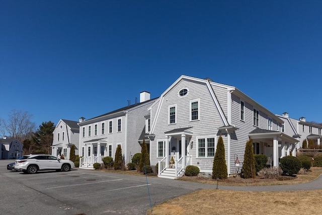 view of front of house featuring uncovered parking, a gambrel roof, and a chimney