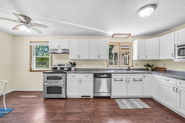 kitchen with appliances with stainless steel finishes, a sink, under cabinet range hood, dark countertops, and a textured ceiling