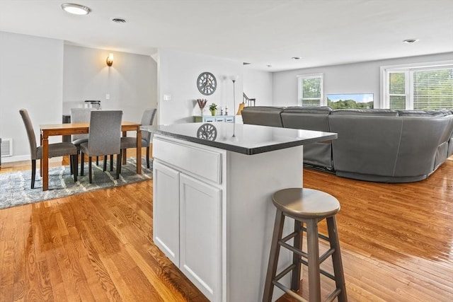 60 Mahogany Run Unit 60, Leominster, MA 01453 - kitchen featuring light wood-style floors, a kitchen island, white cabinets, dark countertops, and a kitchen bar
