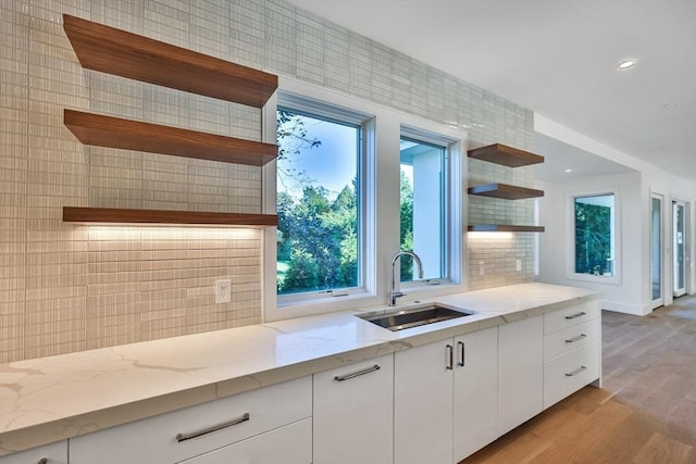 kitchen featuring white cabinetry, sink, backsplash, light stone counters, and light wood-type flooring