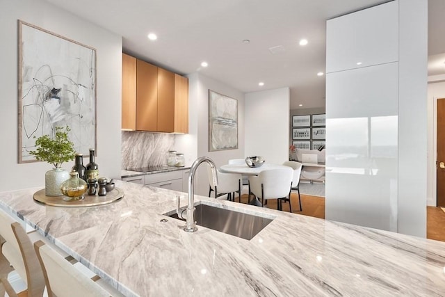 kitchen featuring sink, decorative backsplash, light brown cabinetry, light stone counters, and white cabinetry