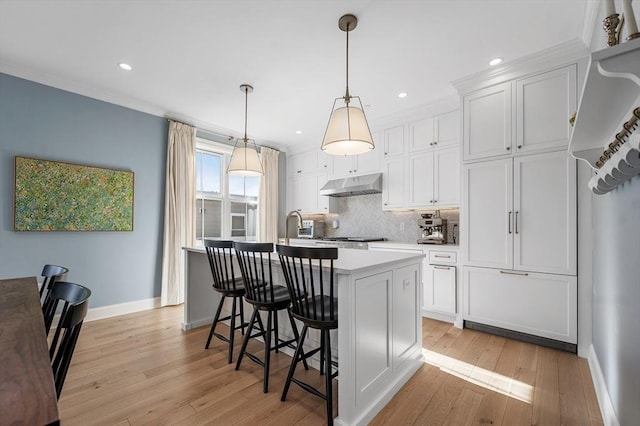 kitchen featuring white cabinets, light hardwood / wood-style floors, a kitchen island with sink, and hanging light fixtures