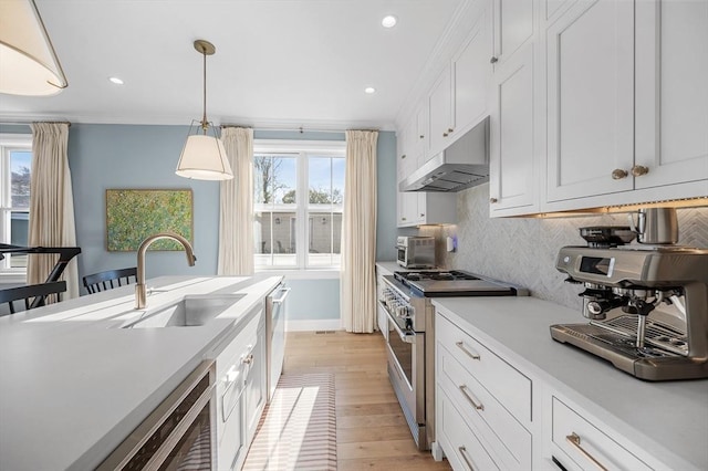 kitchen with pendant lighting, crown molding, sink, high end stove, and white cabinetry