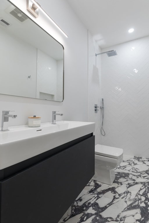 bathroom with toilet, vanity, and tiled shower