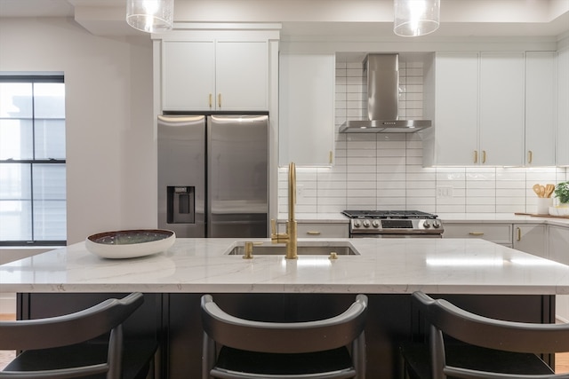 kitchen with sink, wall chimney exhaust hood, stainless steel appliances, a kitchen bar, and white cabinets