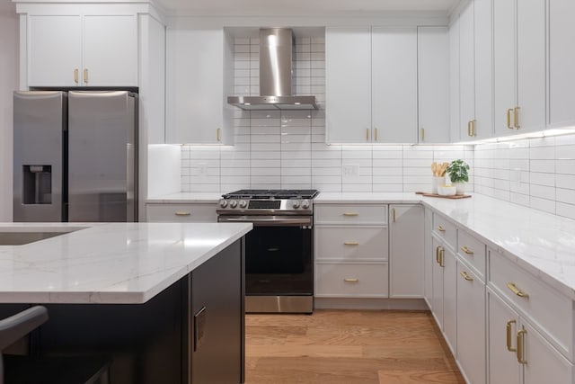 kitchen with wall chimney exhaust hood, light hardwood / wood-style floors, backsplash, and appliances with stainless steel finishes