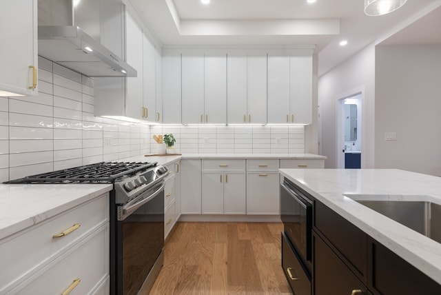 kitchen with white cabinets, wall chimney exhaust hood, light hardwood / wood-style floors, and appliances with stainless steel finishes