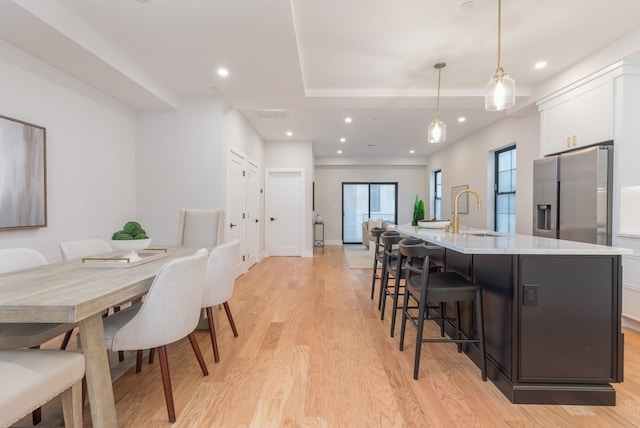 dining room with a tray ceiling, sink, and light hardwood / wood-style flooring