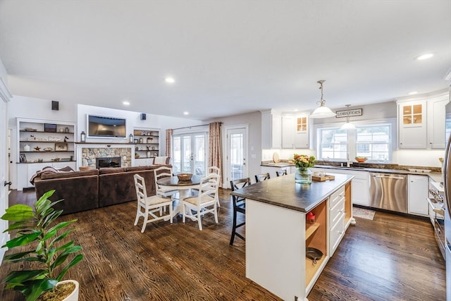 kitchen with pendant lighting, a center island, white cabinets, a stone fireplace, and stainless steel dishwasher