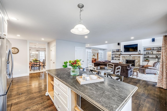 kitchen with stainless steel refrigerator, dark wood-type flooring, a kitchen island, a fireplace, and white cabinets