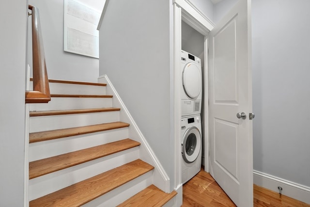 clothes washing area featuring light wood-type flooring and stacked washing maching and dryer