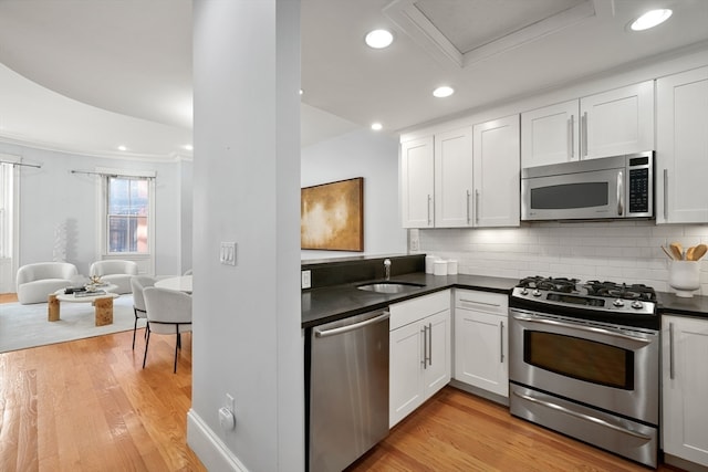 kitchen featuring appliances with stainless steel finishes, tasteful backsplash, crown molding, light hardwood / wood-style floors, and white cabinetry