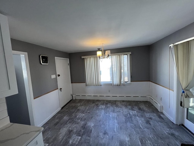 unfurnished dining area featuring dark wood-type flooring, a baseboard radiator, and a chandelier