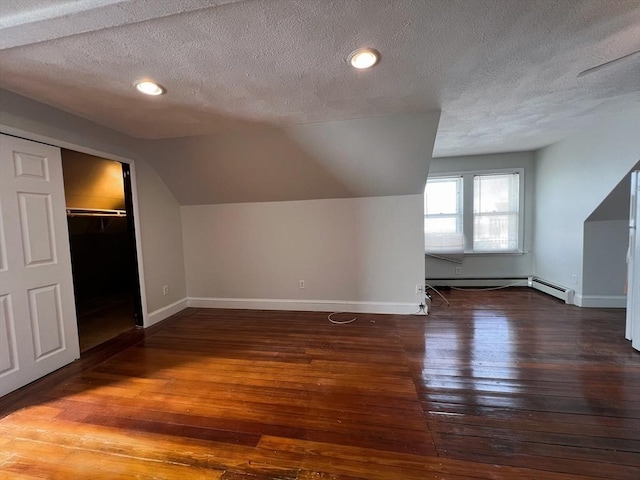 additional living space with a textured ceiling, dark hardwood / wood-style flooring, vaulted ceiling, and a baseboard radiator