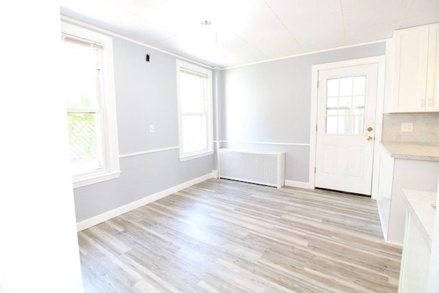 unfurnished dining area featuring radiator, crown molding, and light wood-type flooring