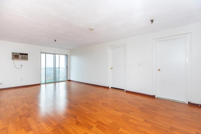 empty room with a wall mounted air conditioner, light wood-style flooring, and baseboards