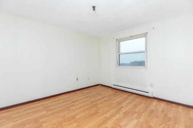 spare room featuring a baseboard heating unit, baseboards, and light wood-style floors