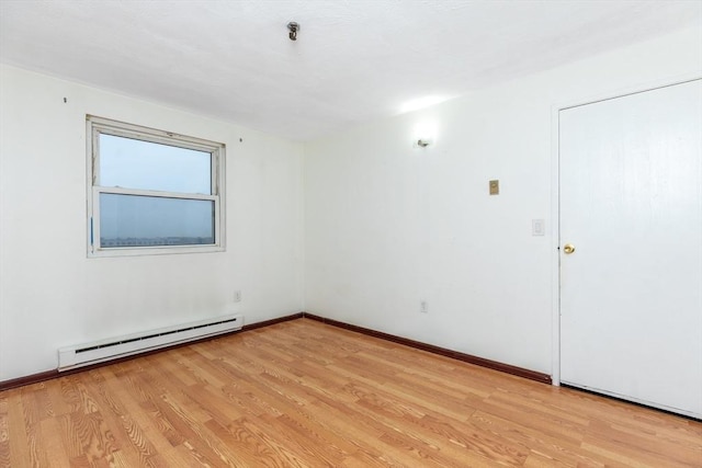 unfurnished room with a baseboard heating unit, light wood-type flooring, and baseboards