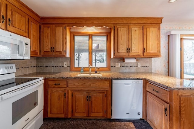 kitchen featuring backsplash, a sink, a peninsula, brown cabinetry, and white appliances