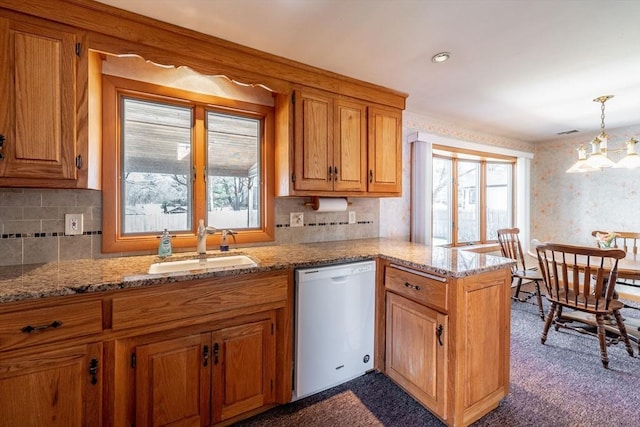 kitchen featuring wallpapered walls, a sink, a peninsula, white dishwasher, and brown cabinets