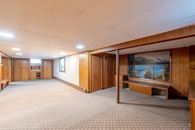 basement with wooden walls, carpet floors, a baseboard heating unit, and a paneled ceiling