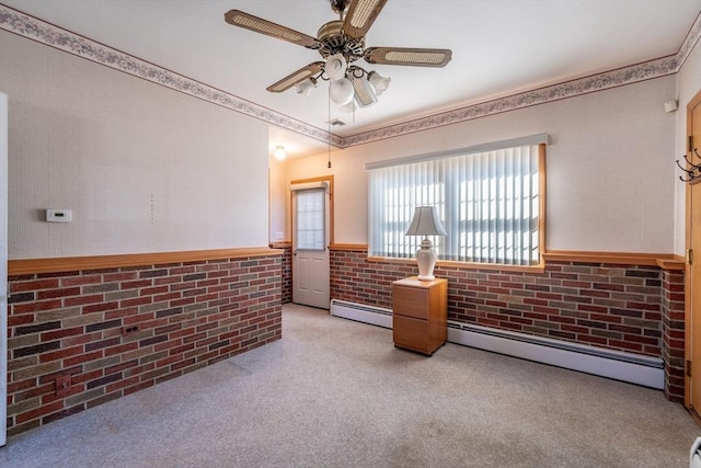 empty room with ceiling fan, baseboard heating, light carpet, brick wall, and wainscoting